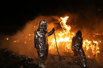Feuerwehrmänner in Schutzkleidung lösen brennende Teile aus einem Brandherd heraus damit das Feuer besser gelöscht werden kann