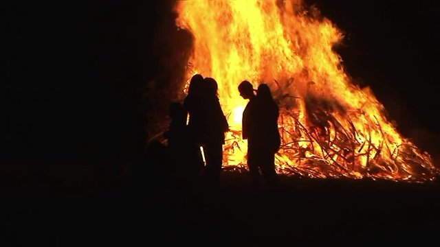 Eine Gruppe von Menschen tummelt sich um das große Osterfeuer in der Finsternis (Kamerazoomfahrt)