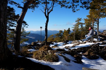 Wanderer genie&szlig;t Aussicht auf Bank in der Sonne und Schnee