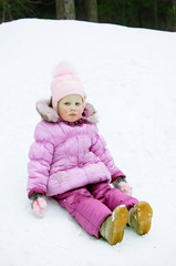 Sad little girl in wet pink clothes sitting in the snow
