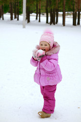 Little girl in pink jacket playing with snow  in winter park