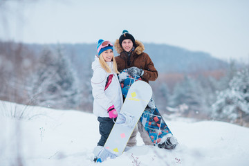 a beautiful young couple snowboarders smiling in the forest