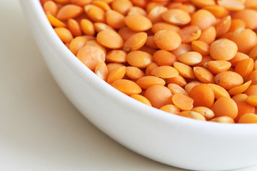 Closeup of raw uncooked red lentils in ceramic spoon on white background