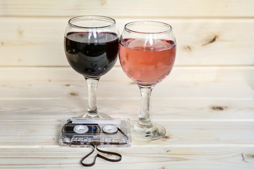 Glasses of red wine , rose and cassette tape isolated on a wooden  background. Romantic date concept 