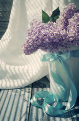 Lilac flowers bouquet in the jug decorated with a blue bow in vintage style. Romantic bouquet of a lilac