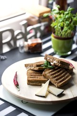 Toasted bread with cheese and ham on a wooden plate decorated with chili peppers, basil and ketchup