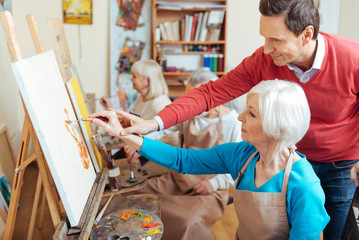 Delighted artist helping elderly woman in painting studio