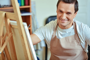 Fototapeta premium Satisfied artist posing in painting studio