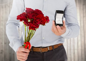 Mid-section of man holding engagement ring and flower bouquet