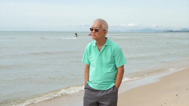 Asian senior man wearing sunglasses and thinking about life planning next to the sea