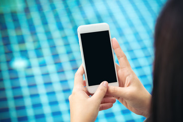 Mockup image of a woman showing smart phone with blank black screen by swimming pool