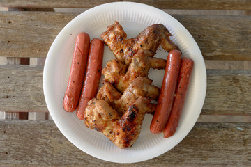 Grilled marinated chicken sausages and wings on white polystyren