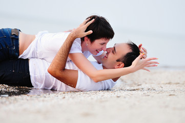 Happy in the arms of a young couple lying on the sand beach