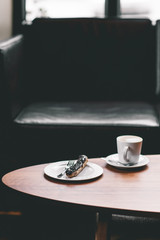 Cup of coffee on wooden table with eclair