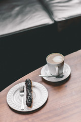 Cup of coffee on wooden table with eclair