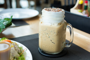 A glass of ice cappuccino art with foods on table