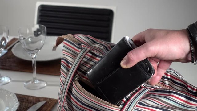 A pickpocket steals the wallet from a bag in a restaurant.