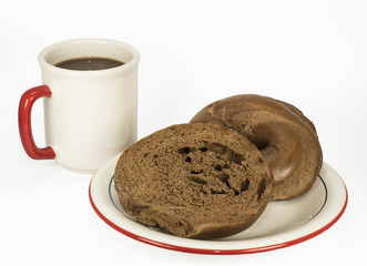 Pumpernickel bagel sliced in half and coffee with white plate and mug trimmed in red and blue on white background