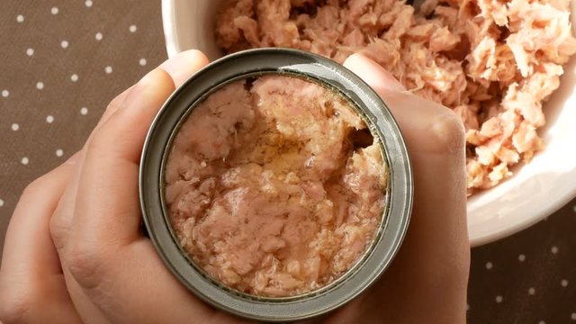 Top view of hand opening canned tuna meat in olive oil.