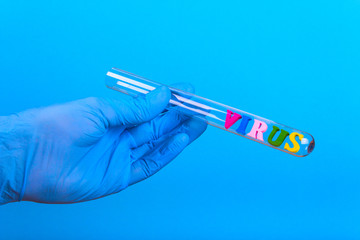 Obraz premium Word virus of colored wooden letters in test-tube. Hand in glove holding a test tube on a blue background