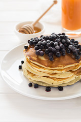Stack of pancakes with frozen blueberries and honey on white wooden table. Selective focus