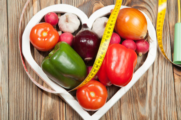 Sport and diet. Vegetables, dumbbells  centimeter. Peppers, tomatoes, garlic, onions,  radishes in the heart on rustic background