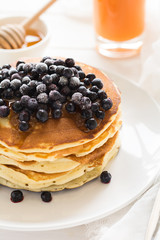 Stack of pancakes with frozen blueberries and honey on white wooden table. Selective focus