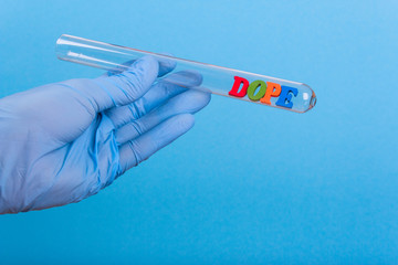 Word dope of colored wooden letters in test-tube. Hand in glove holding a test tube on a blue...