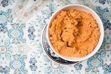 Hummus in the ceramic bowl on the background with patterns top view
