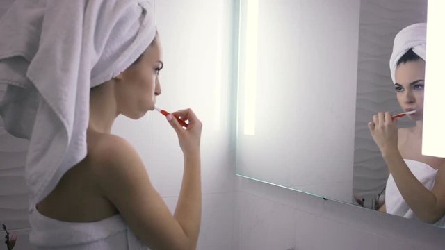 Young woman in a towel brushing her teeth with a toothbrush at the bathroom