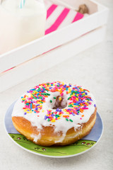 A rainbow sprinkled and frosted donut on a colorful plate.