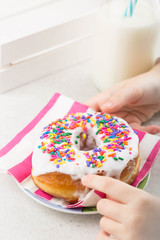 A kid's hands picking rainbow sprinkles from the glazed donut 'doughnut. Milk in the background 