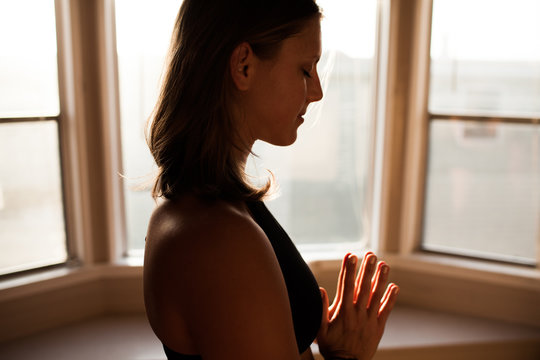 Woman meditating with hands together in sun lit room 