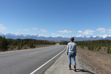 Man going along the highway to the Sayan Mountains in the spring, Buryatia, Siberia, Russia    

