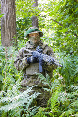 Military man in camouflage uniforms and flak jacket with a gun in the woods