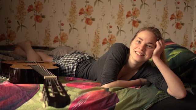 Portrait of beautiful caucasian woman lying in bed and smiling with guitar