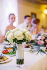Bride's white bouquet stands in a glass on dinner table