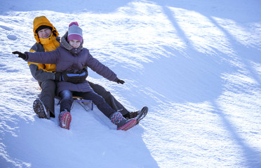 Dad and daughter sledding on a sunny day.