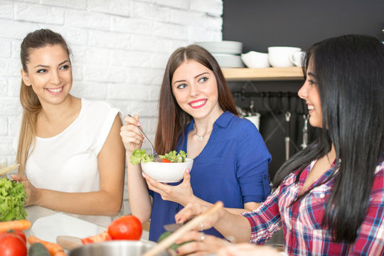 Young woman eating a fresh salad and talking with her friends in the kitchen.