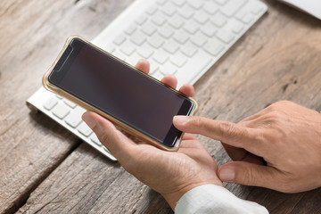 Man holding and using smart phone .
Close up of businessman touching screen of smart phone at old wooden table together with keyboard and mouse desktop computer.