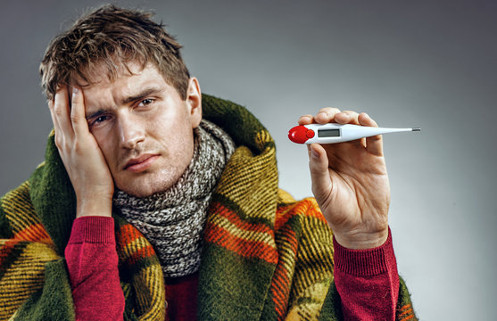 Sick man shows the temperature on the thermometer. Young man suffering cold and winter flu virus. Health care concept