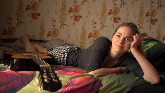 Portrait of beautiful caucasian woman lying in bed and smiling with guitar
