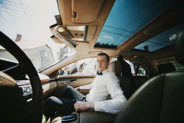 Man in white shirt and black bow tie sits in car with panoramic