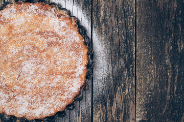Homemade pie sprinkled with powdered sugar on rustic wooden background. Space for text.