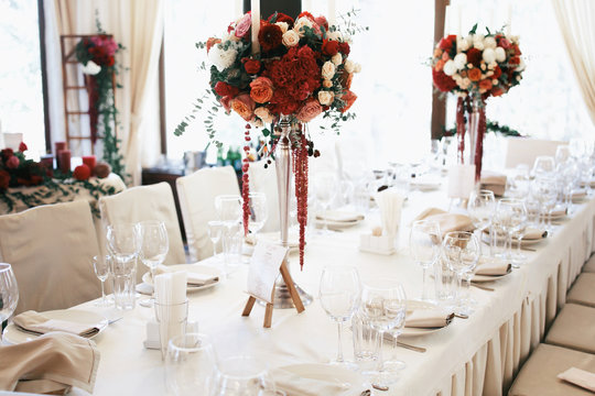 Tall steel vases with red bouquets stand on long beige table