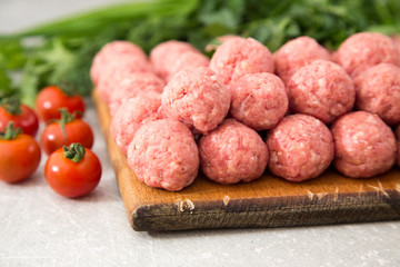 Raw meatballs on a rustic wooden cutting board on a stone backgr