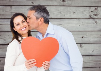 Mature man kissing a woman holding red heart