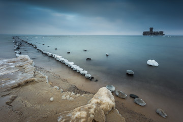 Winter landscape at the sea. Frozen wooden breakwaters line to the world war II torpedo platform (polish name torpedownia ) at Baltic Sea.  Morning at Babie Doly, Poland. Long exposure photo.