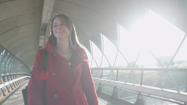 Beautiful woman walking in the city and smiling. The sun is coming in the lens.