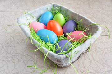 Easter wicker basket with colored eggs on white board.